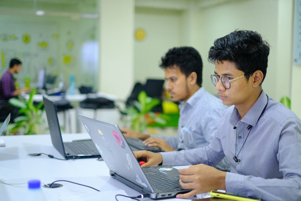 Two young professionals working on laptops in a vibrant and modern office setting.